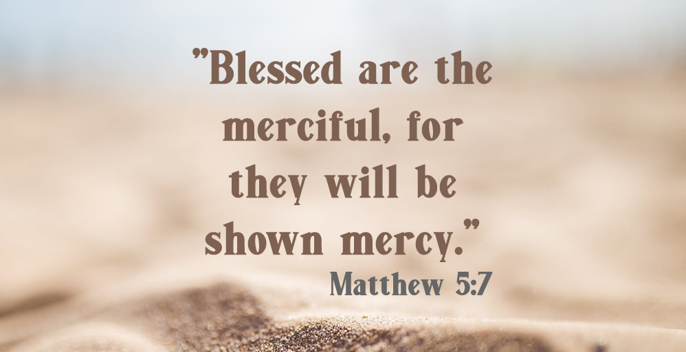 Matthew 5:7 on sand background