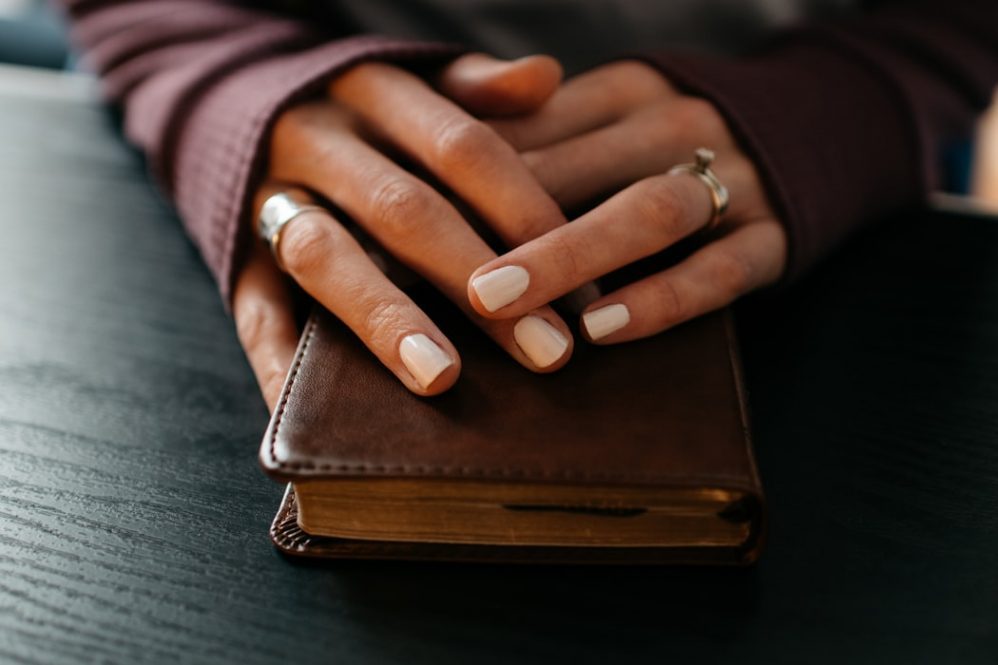 Woman's praying hands resting on top of a Bible